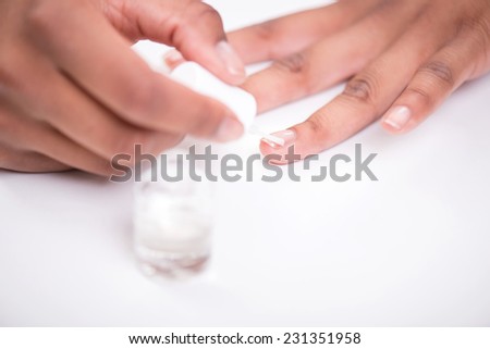 Girl  with beautiful hands painting her short nails with transparent enamel  sitting at white table  isolated on white background close up