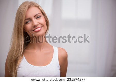 Close up portrait of beautiful blond girl with green  eyes  and straight  hair in white  T shirt  looking at camera smiling   with copy place