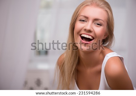 Portrait of beautiful happy blond girl with green  eyes  and straight  hair in white  T shirt  looking at camera smiling opening her mouth   with copy place