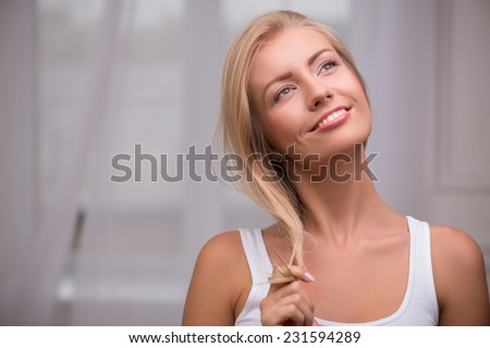 Portrait of beautiful blond girl with green  eyes  and straight  hair in white  T shirt  looking aside smiling dreaming touching her hair    with copy place