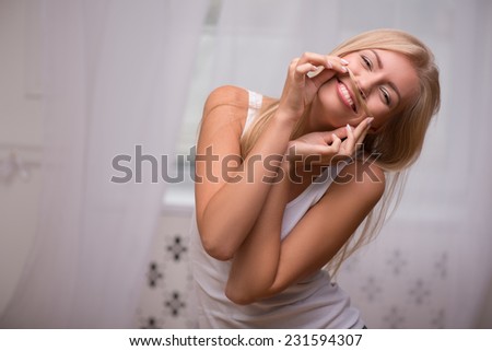 Portrait of beautiful  funny nice happy blond girl with green  eyes  and straight  hair in white  T shirt  looking at camera holding hair as moustache   waist up