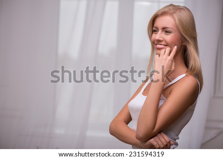 Beautiful  happy blond girl with green  eyes  and straight  hair in white  T shirt  looking aside  smiling   with copy place waist up