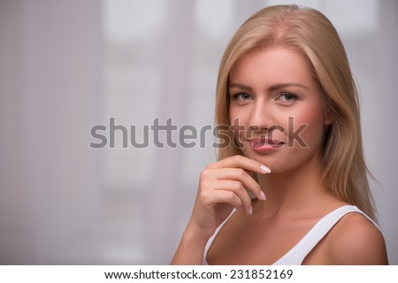 Portrait of beautiful  blond girl with green  eyes  and straight  hair in white  T shirt  looking at camera smiling touching her face   with copy place
