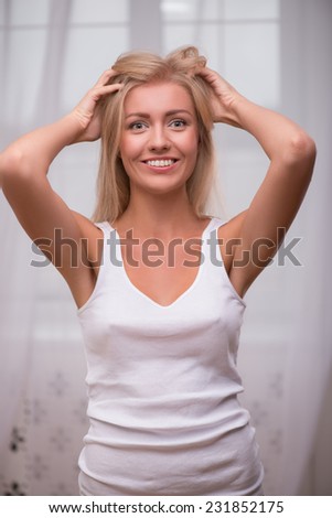 Beautiful blond girl in white  T shirt  looking at camera smiling opening mouth tousling her hair smiling  holding head with hands waist up