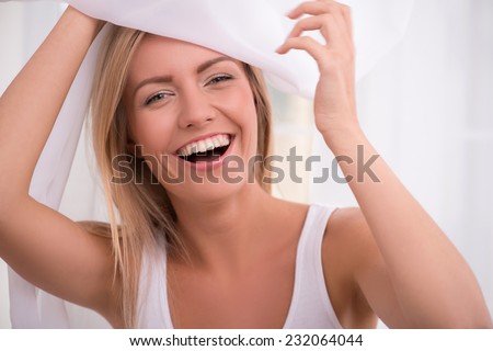 Portrait of beautiful fun happy  blond girl with green  eyes  and straight  hair in white  T shirt  looking  out curtain