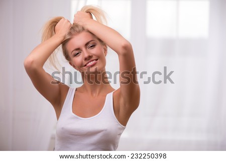 Portrait of beautiful blond girl in white  T shirt  looking at camera smiling opening mouth tousling her hair with hands