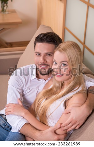 Portrait of happy couple in love of handsome man and attractive woman sitting on sofa embracing looking at camera waist up