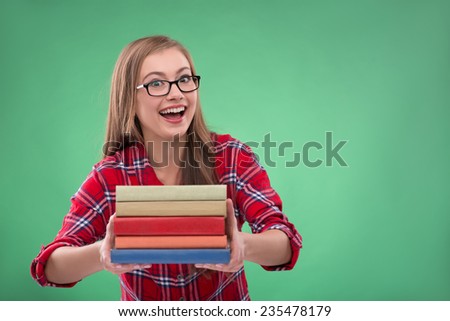 Portrait of beautiful happy brown haired girl in  glasses with books  on green background smiling looking at camera waist up with copy place