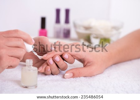 manicurist doing manicure  client  painting nails with transparent nail polish  in salon  on white towel