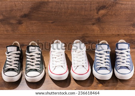 three pairs of cool youth white gym shoes with red  stripes  on brown wooden floor  standing in line with copy place  top view