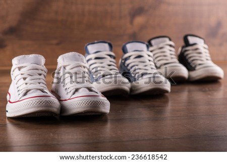 three pairs of cool youth white gym shoes with red  stripes  on brown wooden floor  standing in line with perspective and  selective focus