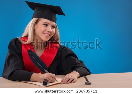 Portrait of beautiful happy blond girl in black cloak and master hat writing with ink and feather smiling  with copy place