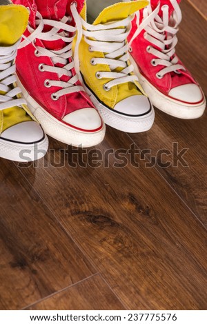 two pairs of cool youth red and yellow  gym shoes white laces   on brown wooden floor  standing in line with copy place