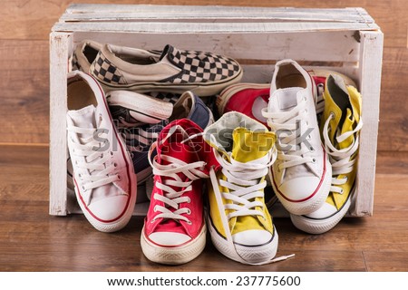 several  pairs of cool youth red blue white yellow  gym shoes falling out white  box   on brown wooden floor