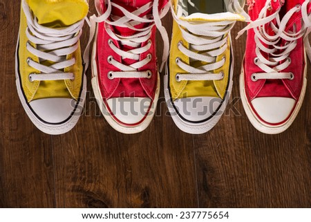 two pairs of cool youth red and yellow  gym shoes white laces   on brown wooden floor  standing in line with copy place  top view