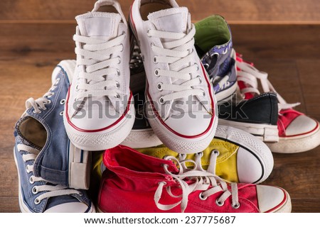 heap of several  pairs of cool youth red blue white yellow  gym shoes   on brown wooden floor