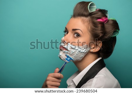 Cute funny  brunette woman in hair curlers wearing men shirt and tie undone posing with foam on face, isolated on blue background, role gender reversal concept