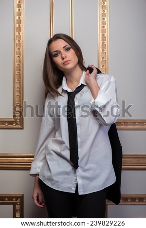 Full length portrait of young sexy woman wearing men suit oversize and tie holding jacket behind  her back, provocative look, interior shot