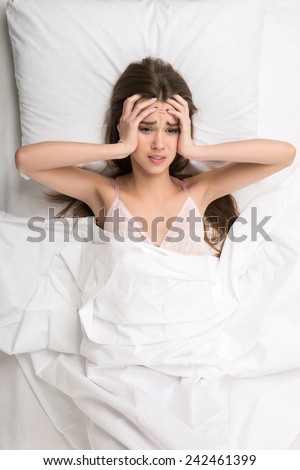 Too much noise. Beautiful young woman touching her head because of noise while lying on the bed