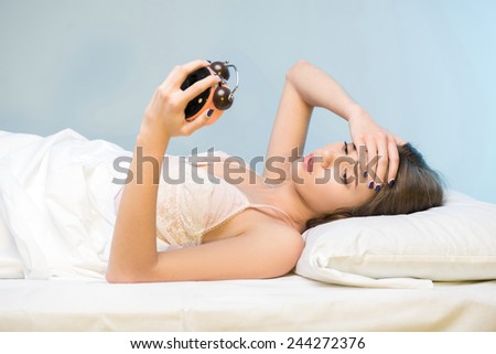 Insomnia. Side view portrait of young thoughtful beauty looking at the clock while lying in bed
