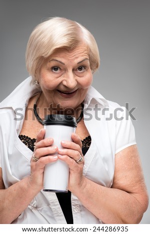 Taking some time for myself. Smiling senior woman holding white thermos cup while standing against grey background
