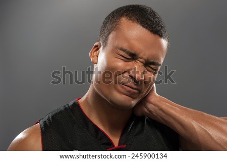 Feeling neckache after workout. Frustrated young African man touching his neck and expressing negativity while standing against grey background