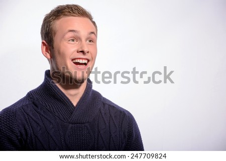 Wow. Surprised young man in cardigan looking away with his mouth open while standing against white background