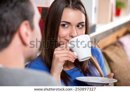Carefree time in cafe. Beautiful young couple looking at each other and smiling while enjoying coffee in cafe together with selective focus