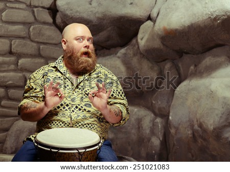 Love the beat. Portrait of funny bearded man playing the drum and showing OK sign while sitting against stonewall background