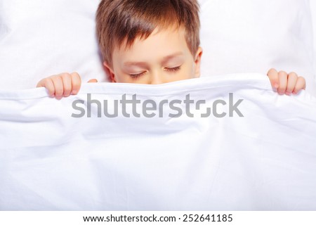 Peaceful sleep.  Top view of an adorable little boy sleeping in bed covering his face with white blanket with copy space