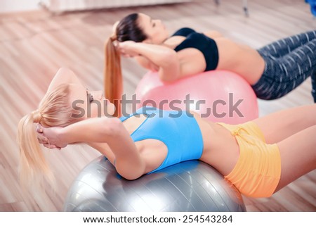 Take it to the next level. Two beautiful young women in sports clothing exercising together on fit balls at the gym