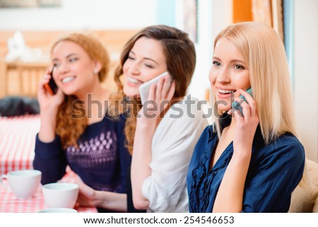 No minute without technologies. Three young beautiful female friends sitting in cafe and talking over their cell phones