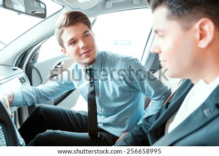 Perfect car salesman and customer. Closeup of  young professional salesman in formalwear sitting in the car with a smiling client