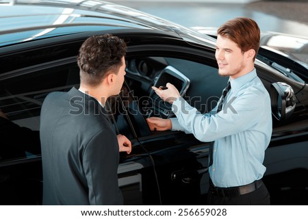 Salesman and customer. Top view of a handsome young classic car salesman talking to a customer and smiling while standing in car dealership