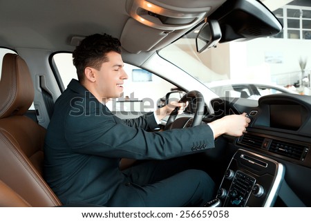 Let us go for a ride. Handsome young businessman examining the car at the dealership while sitting inside the new car and touching the steering wheel