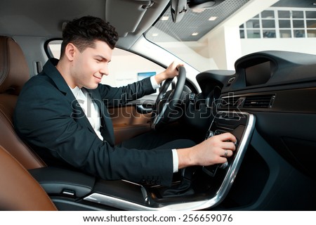 Let us go for a ride. Handsome young businessman examining the car at the dealership while sitting inside the new car and touching the gear box