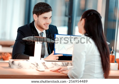 Business team at lunch. Handsome young man in suit pointing at clipboard with analytics while sitting at the restaurant with his colleague