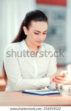 Checking business messages. Confident young woman in formalwear drinking coffee and looking at her mobile phone while sitting at bar counter