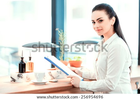 Confident and successful business lady. Side view of beautiful young woman in formalwear looking at clipboard with analytics while sitting at the restaurant