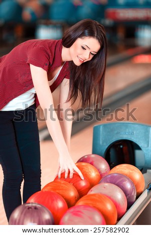 Choosing a ball. Cheerful young women choosing bowling ball and smiling while standing against bowling alleys