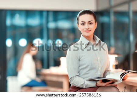 Successful business lady. Beautiful young woman in formalwear holding a corporate magazine and smiling while leaning at bar counter