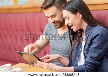 Surfing in the net. Side view of attractive young couple looking at digital tablet and smiling at camera while sitting in the cafe