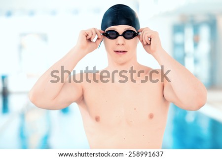 Born to swim.  Young handsome man with naked torso wearing a swimming cap and goggles while standing in the swimming pool