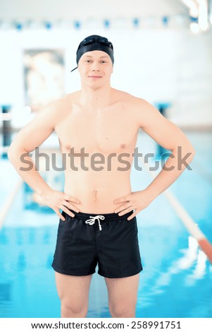 Born to swim.  Young handsome man with naked torso wearing a swimming cap and goggles standing in the swimming pool with his hands on hips