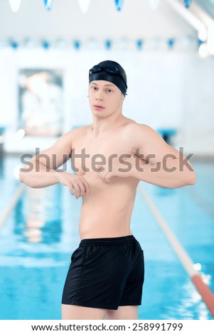 Getting ready to win. Young handsome man with naked torso wearing a swimming cap and goggles getting ready to start a swim while standing in the swimming pool