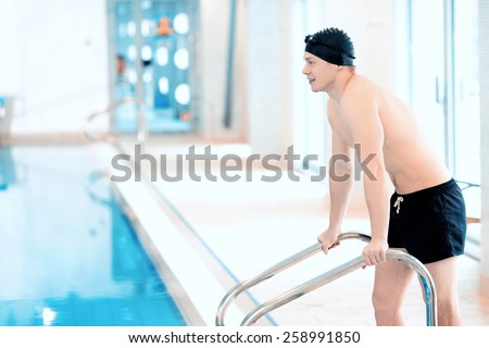 On the way in. Side view of young handsome man with naked torso wearing a swimming cap and goggles going down to the swimming pool