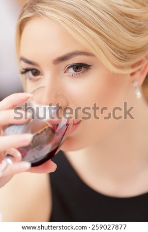 Making a toast. Closeup of beautiful young woman in dress drinking wine while having dinner in luxury restaurant