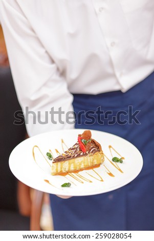 Try our tasty specials. Closeup shot of exquisite dessert on the plate in hands of waiter in uniform in the luxury restaurant