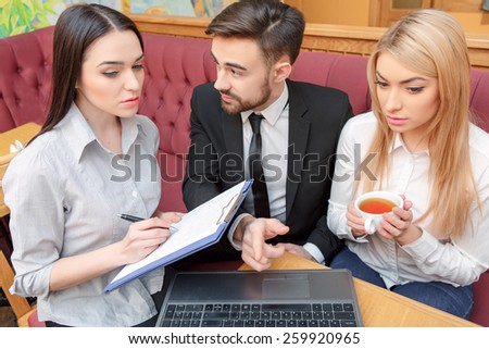 Business team at lunch. Top view of handsome young man and his female colleagues in formalwear looking at laptop and pointing at screen while sitting at the restaurant