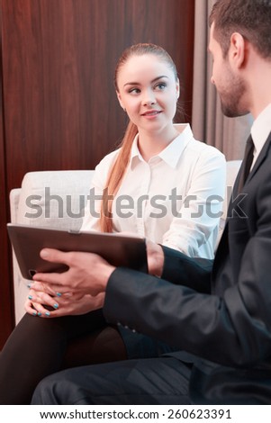 Business in digital age. Two cheerful business people in formalwear discussing something and smiling while one of them sitting from behind pointing digital tablet